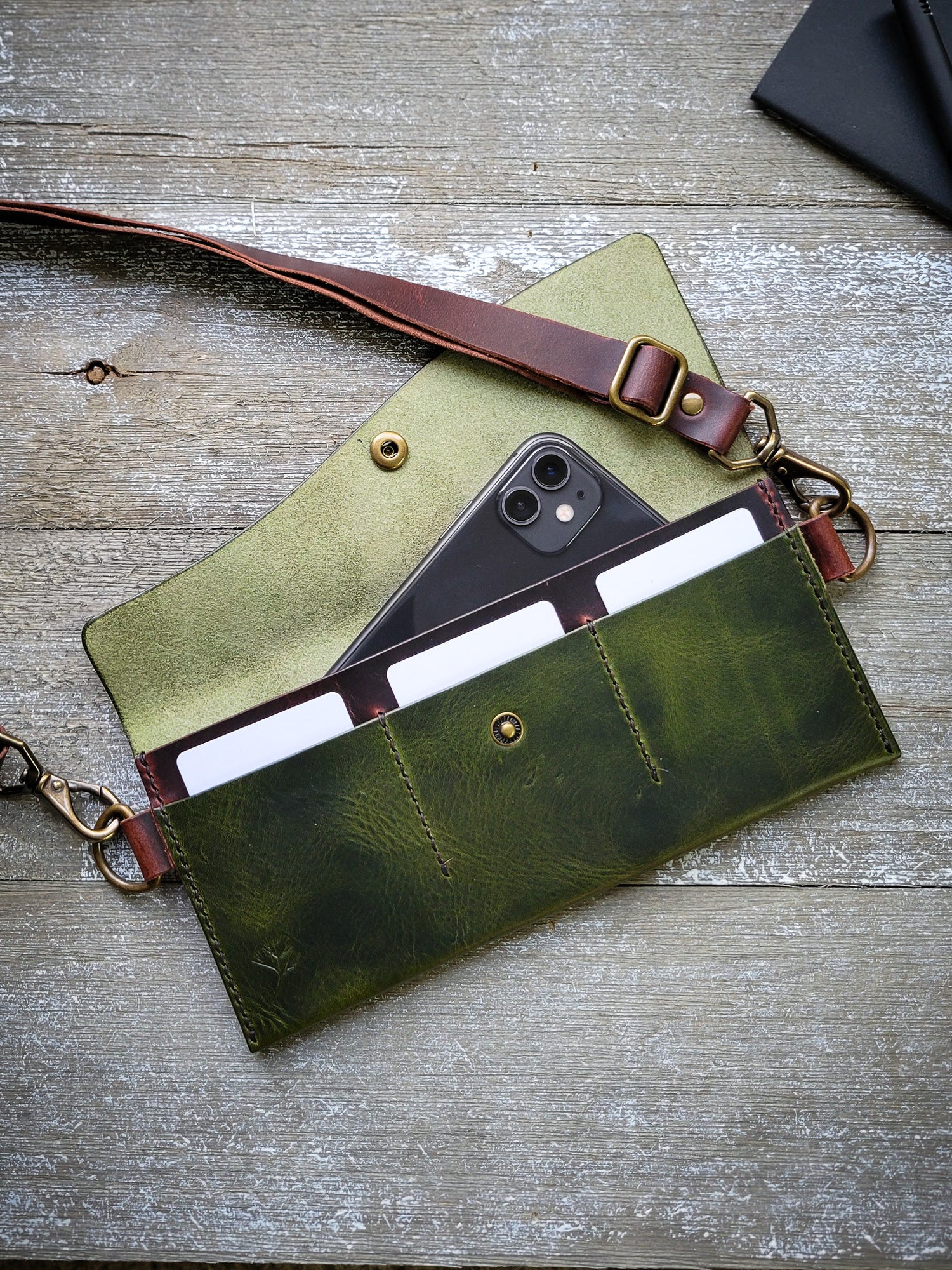 Green leather clutch with a phone inside on a wooden surface