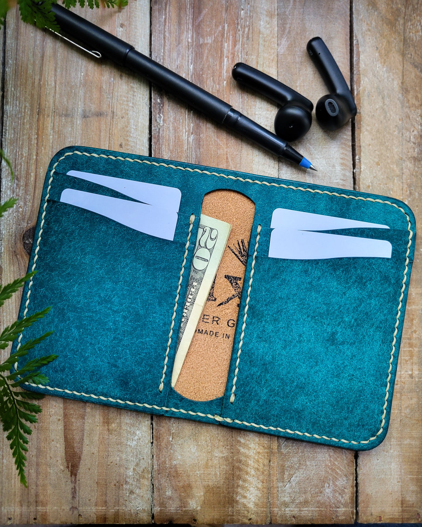 Blue leather vertical bifold wallet on a wooden background with pen and earbuds