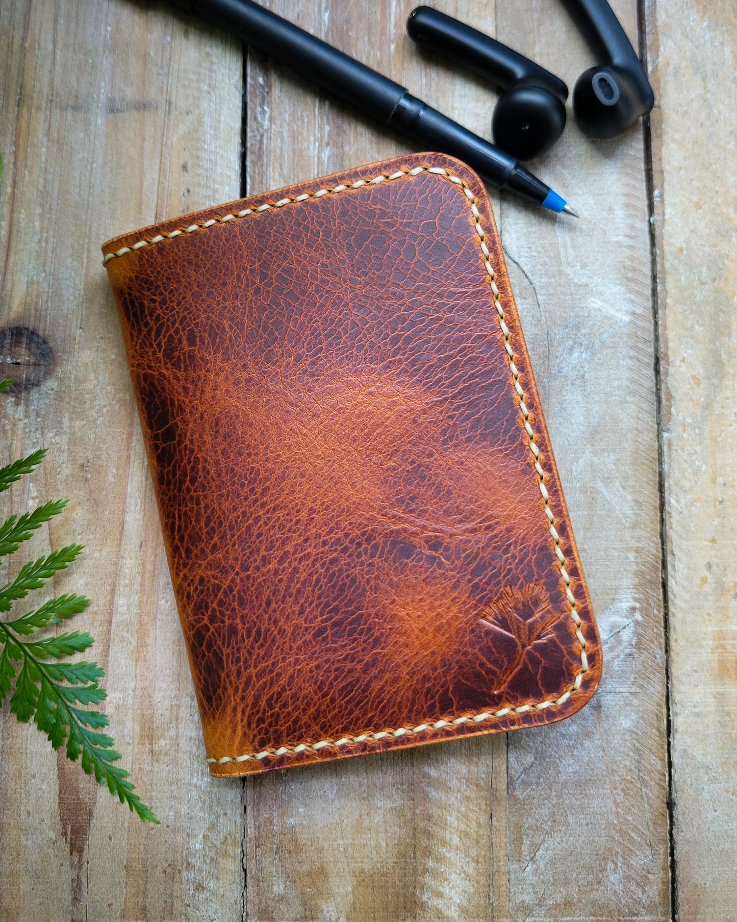 Brown leather wallet on a wooden surface with a pen and small container.