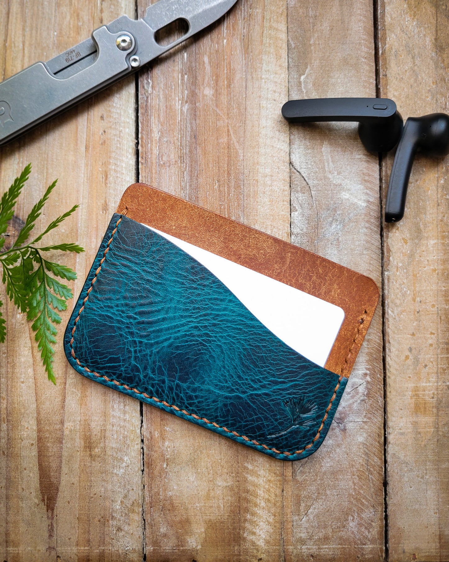 Blue leather cardholder on a wooden surface with a knife and tool in the background