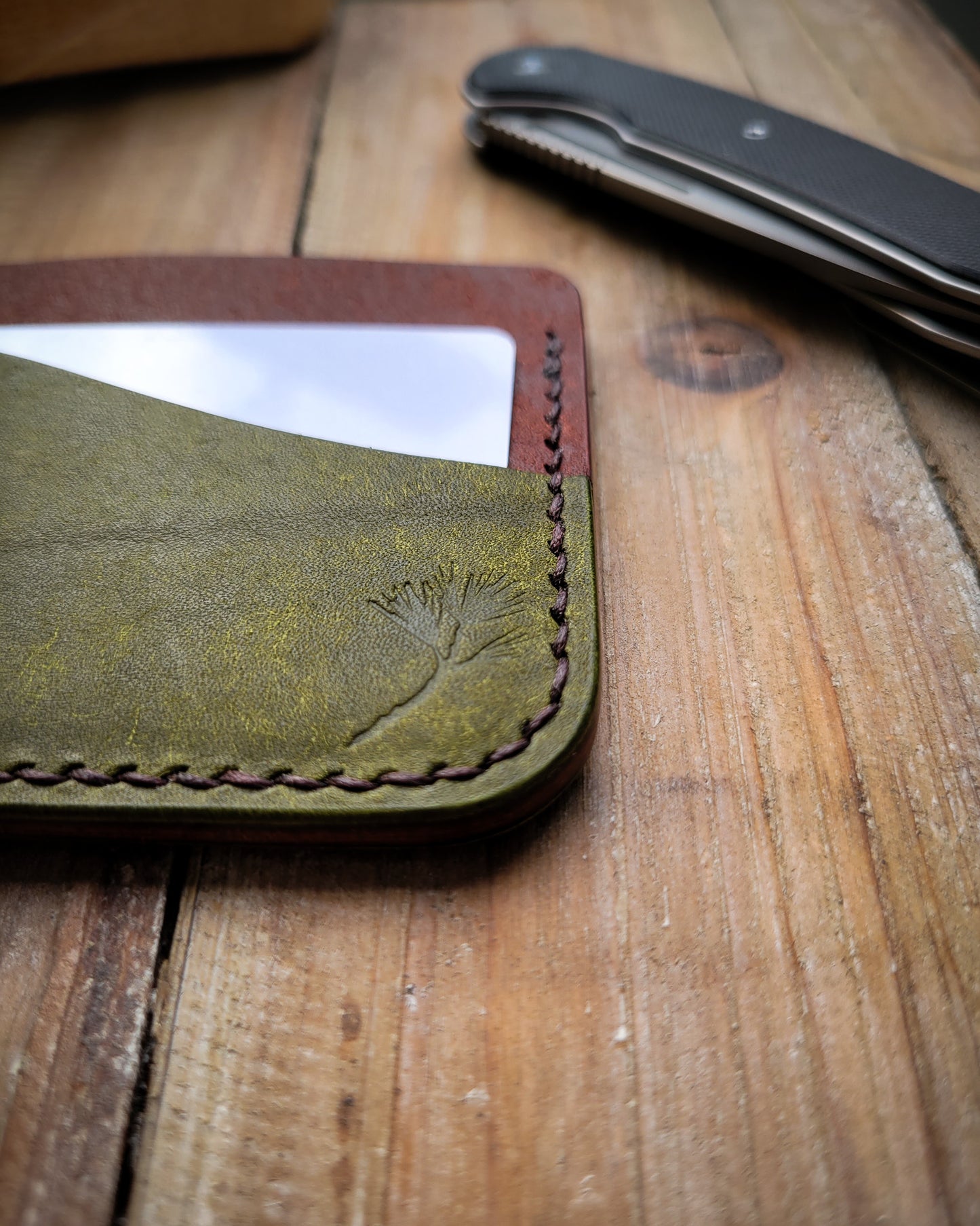 Green leather wallet with pine branch design on a wooden surface