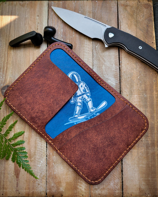 Brown leather wallet with astronaut liner and a knife on a wooden background