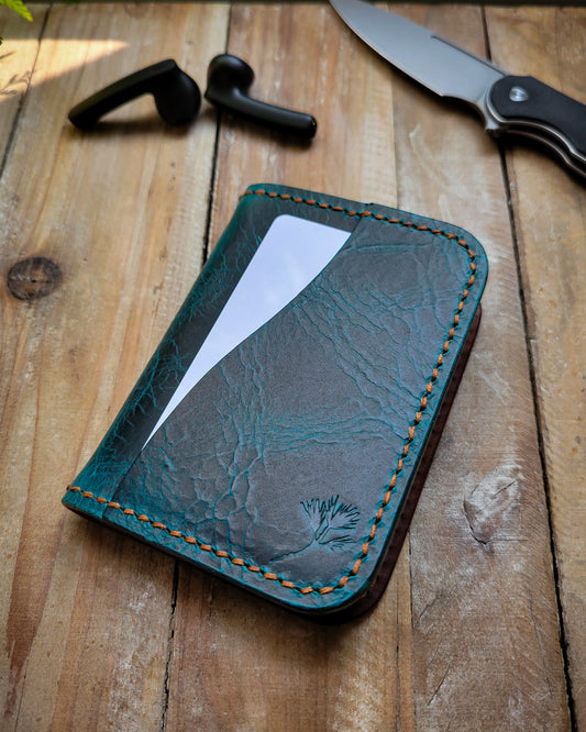 Blue leather wallet with white card on a wooden surface with a knife and earbuds.