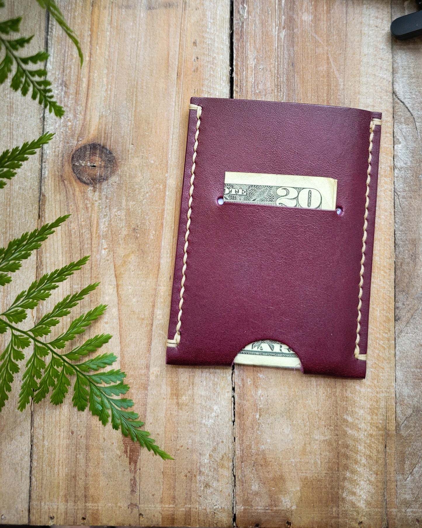 Purple ultralight minimalist wallet with cream stitching. It is holding a folded $20 bill and four cards.