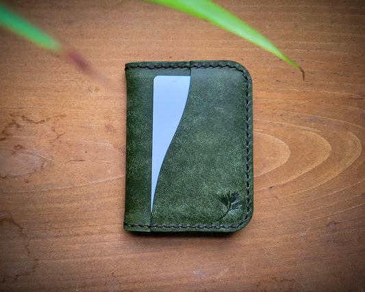 Green Pueblo Leather minimalist wallet with external card pocket sitting closed on top of distressed wood. 