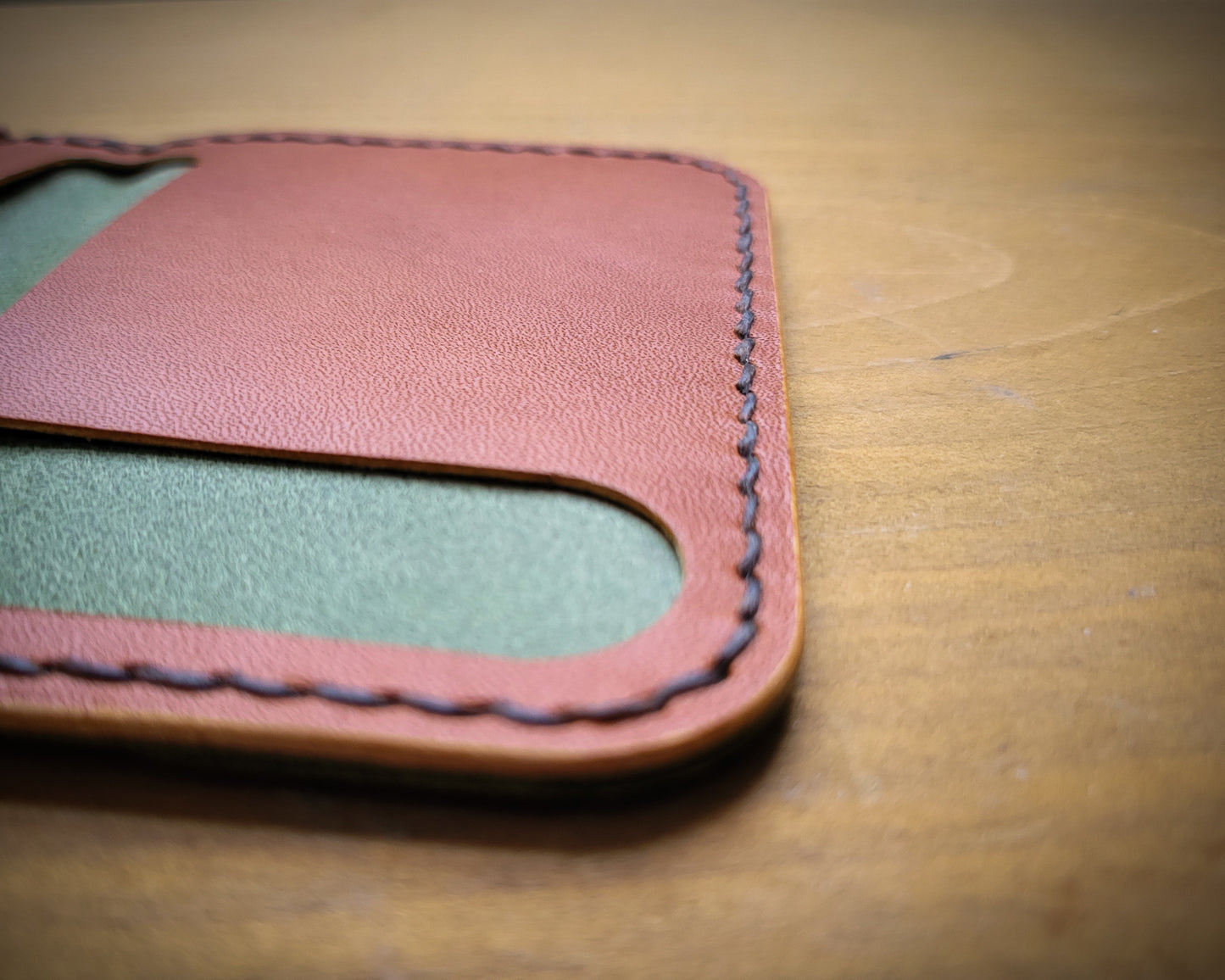 Closeup image of the tan Wickett & Craig interior of a green Pueblo Leather minimalist wallet. The image is focused on the brown thread saddle stitching
