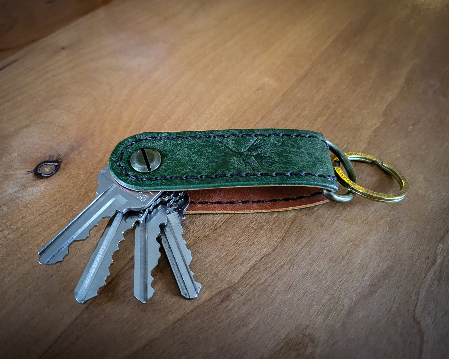 Green Leather EDC Key Organizer stitched with brown thread holding 4 keys. Laying open on wood table. 