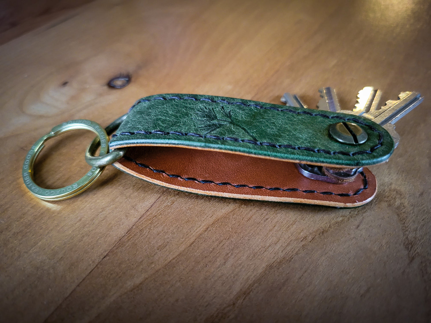 Green and Brown Leather EDC Key Organizer stitched with brown thread holding 4 keys. laying open on wood table.