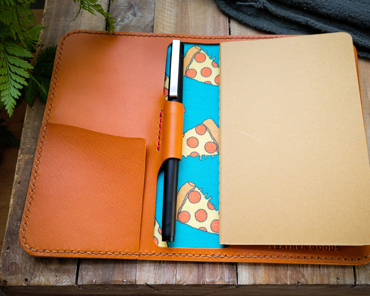 Tan leather notebook with red accent stitching and lined with pepperoni pizza fabric.