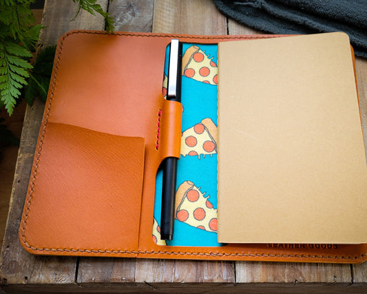 Tan leather notebook with red accent stitching and lined with pepperoni pizza fabric. 
