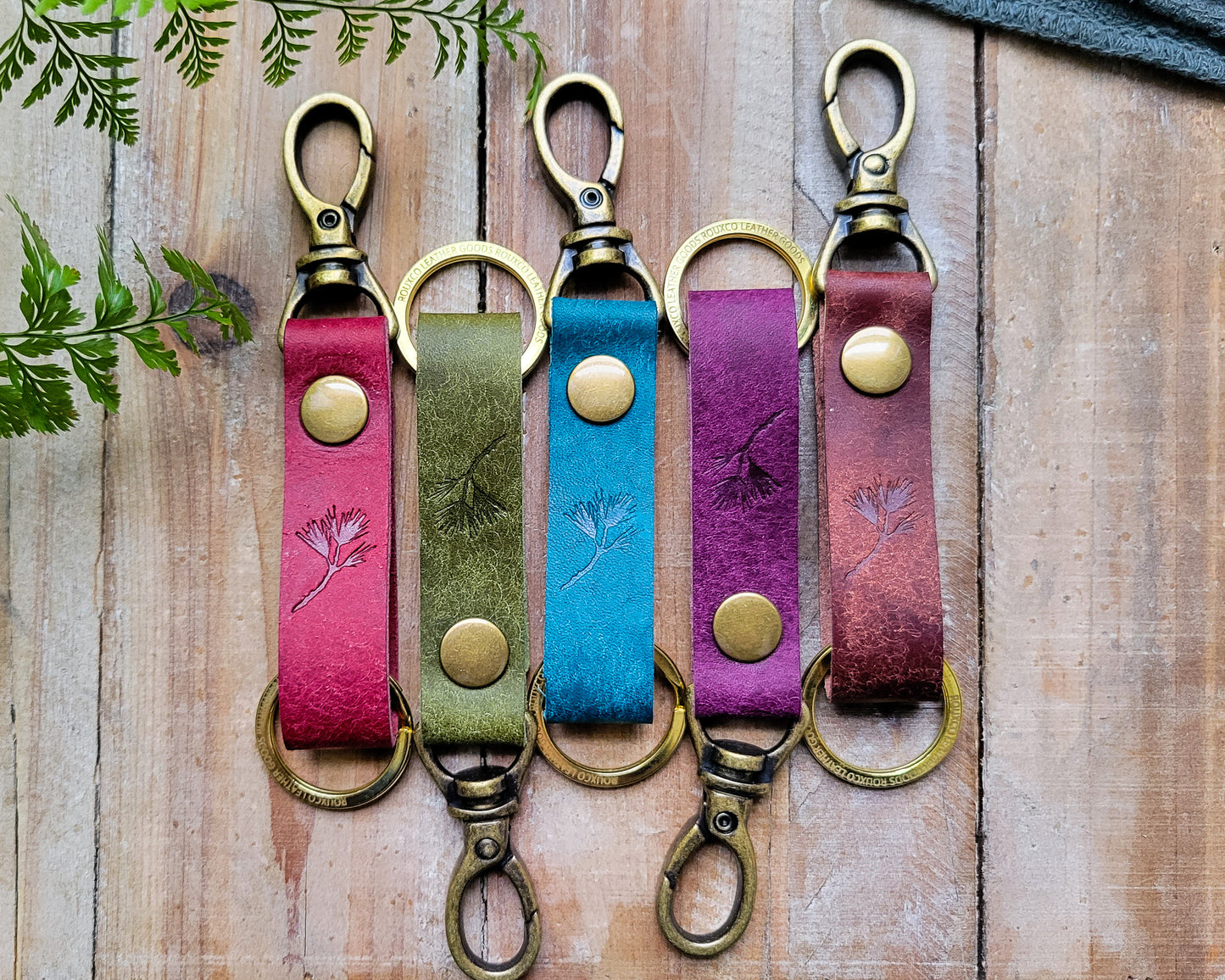 Five Italian leather key clips in multiple colors with brass hardware laying on a rustic wooden table. 