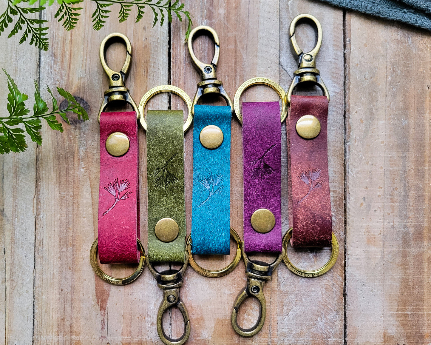 Five Italian leather key clips in multiple colors with brass hardware laying on a rustic wooden table.