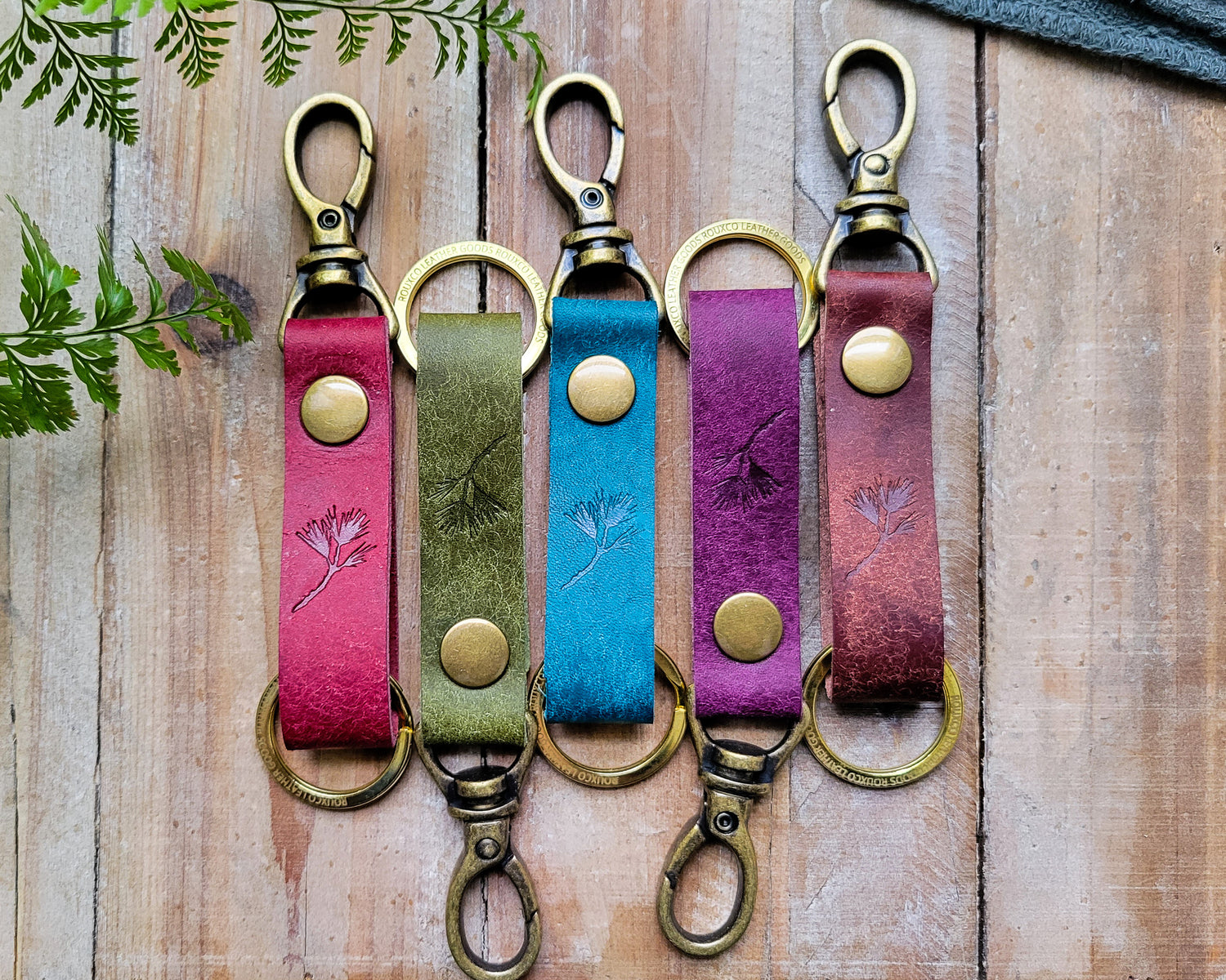 Five Italian leather key clips in multiple colors with brass hardware laying on a rustic wooden table.