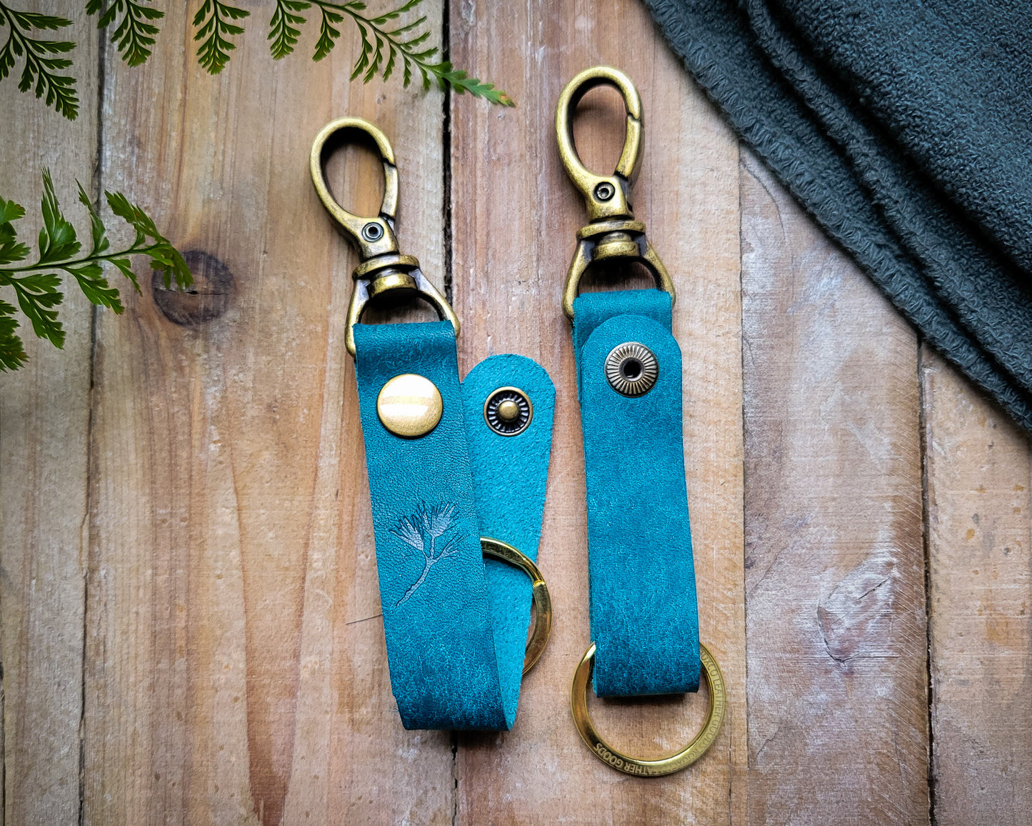 Blue italian leather key clip with brass hardware laying on a rustic wooden table.