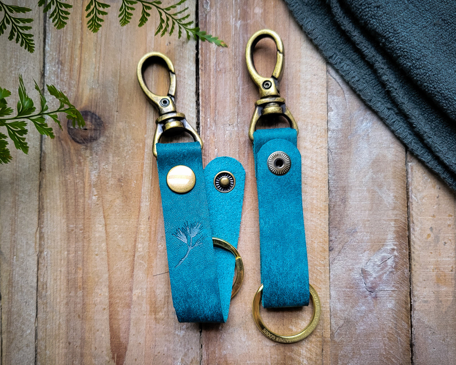 Blue italian leather key clip with brass hardware laying on a rustic wooden table.