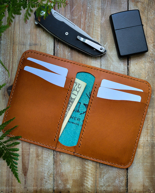 Brown leather wallet with card slots on a wooden surface with a knife and lighter.