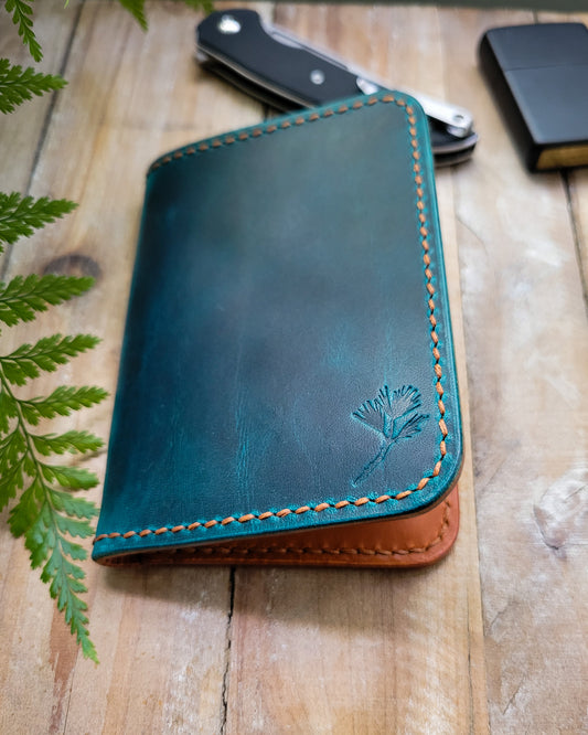 Blue leather wallet with brown stitching on a wooden surface with a plant in the background