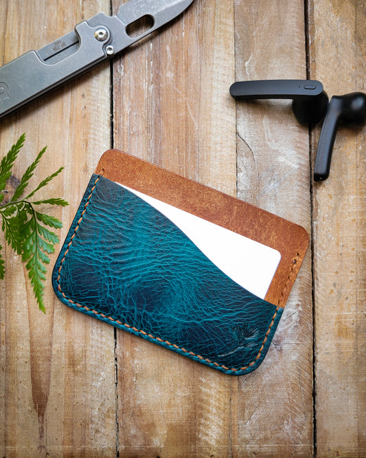 Blue leather cardholder on a wooden surface with a knife and tool in the background