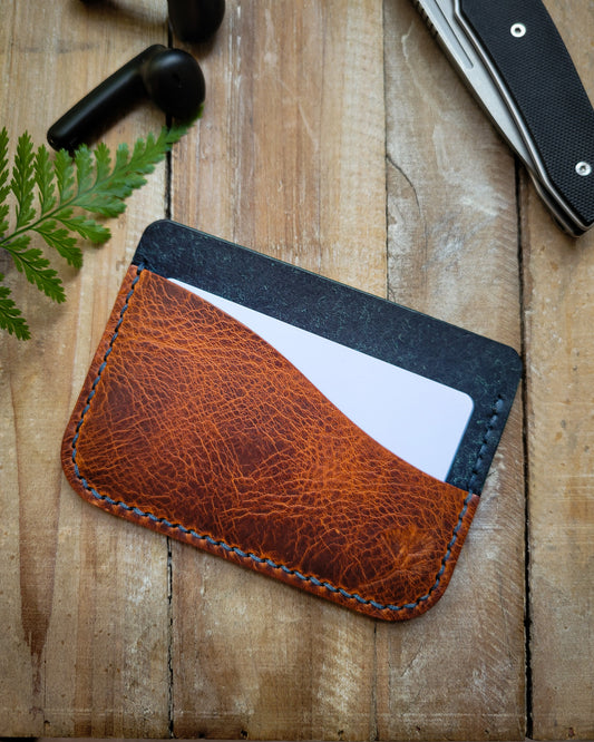 Brown leather cardholder on a wooden surface with a plant and knife in the background