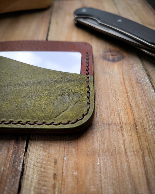 Green leather wallet with pine branch design on a wooden surface