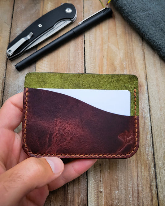 Hand holding a leather cardholder with a pen and knife in the background on a wooden surface