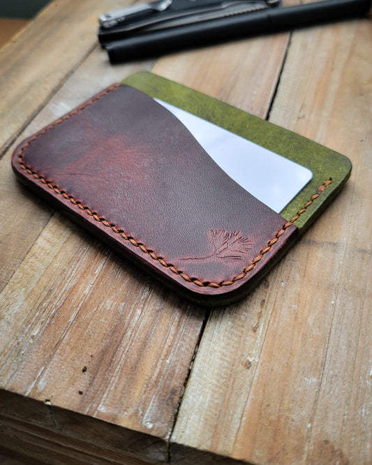 Green and brown leather wallet with a card on a wooden surface