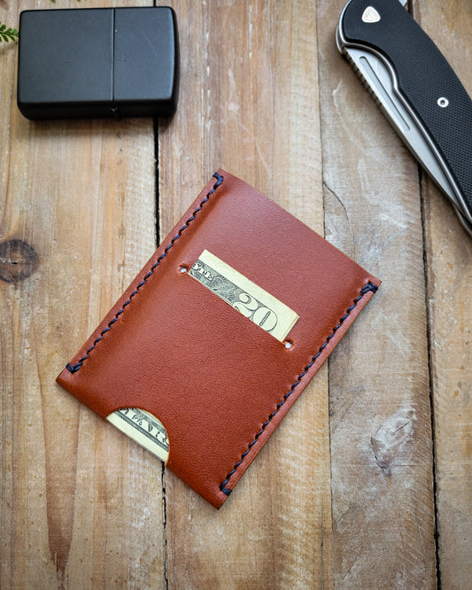 Brown leather wallet with folded cash on a wooden surface with a lighter and knife.
