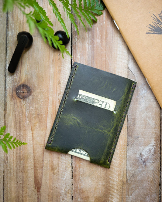 Green leather wallet on a wooden surface with leaves and a brown notebook.