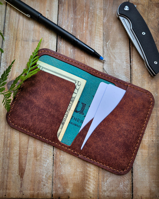 Brown leather wallet with cards on a wooden surface with a pen and knife.