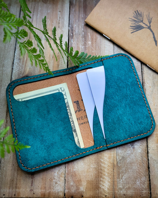 Teal leather wallet with card slots on a wooden surface with plants