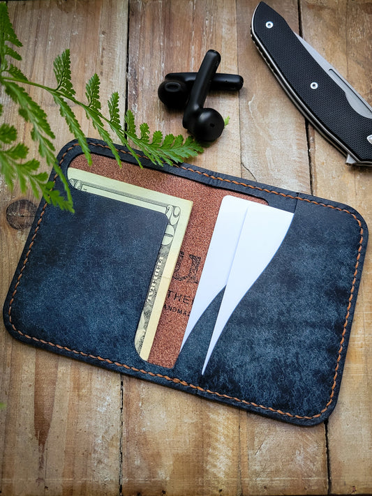 Blue leather wallet with money and cards on a wooden surface with a plant and knife in the background