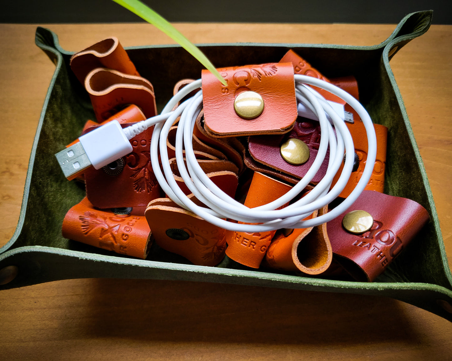 Tan and Brown Wickett & Craig cable organizers with brass button snaps. They are sitting in a green Pueblo Leather EDC Tray.